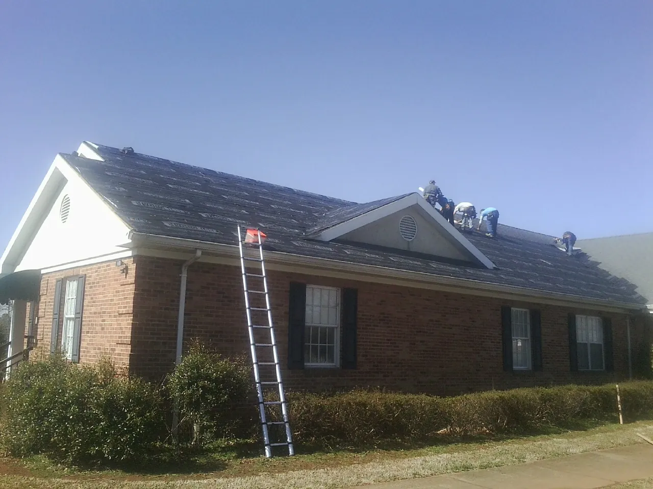 Crew tearing shingles off a brick ranch roof with a ladder set — Metal Roof Repair work by our crew in Dowagiac