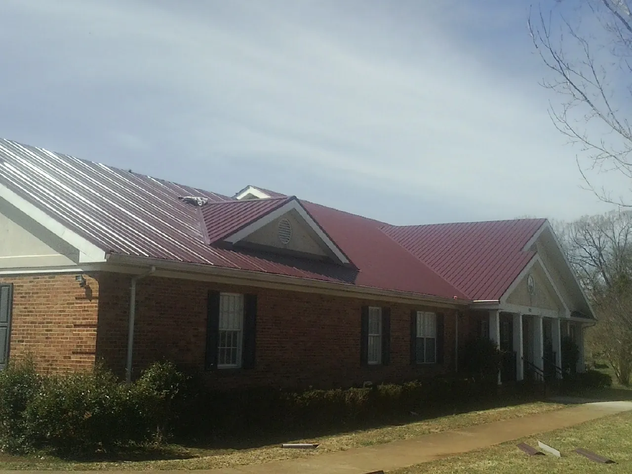 Red metal roof with gabled entries on a long brick building, from a Hail Damage Roof Repair job in Dowagiac