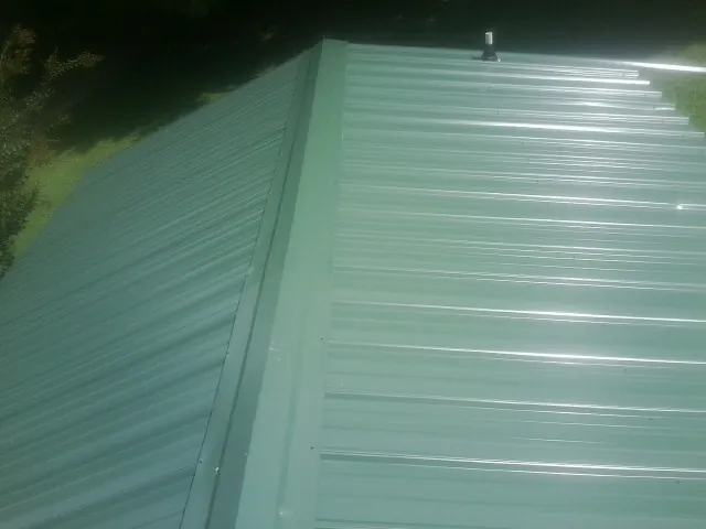 New green metal panels meeting at the ridge of a roof — Flat Roof Repair work by our crew in Dowagiac