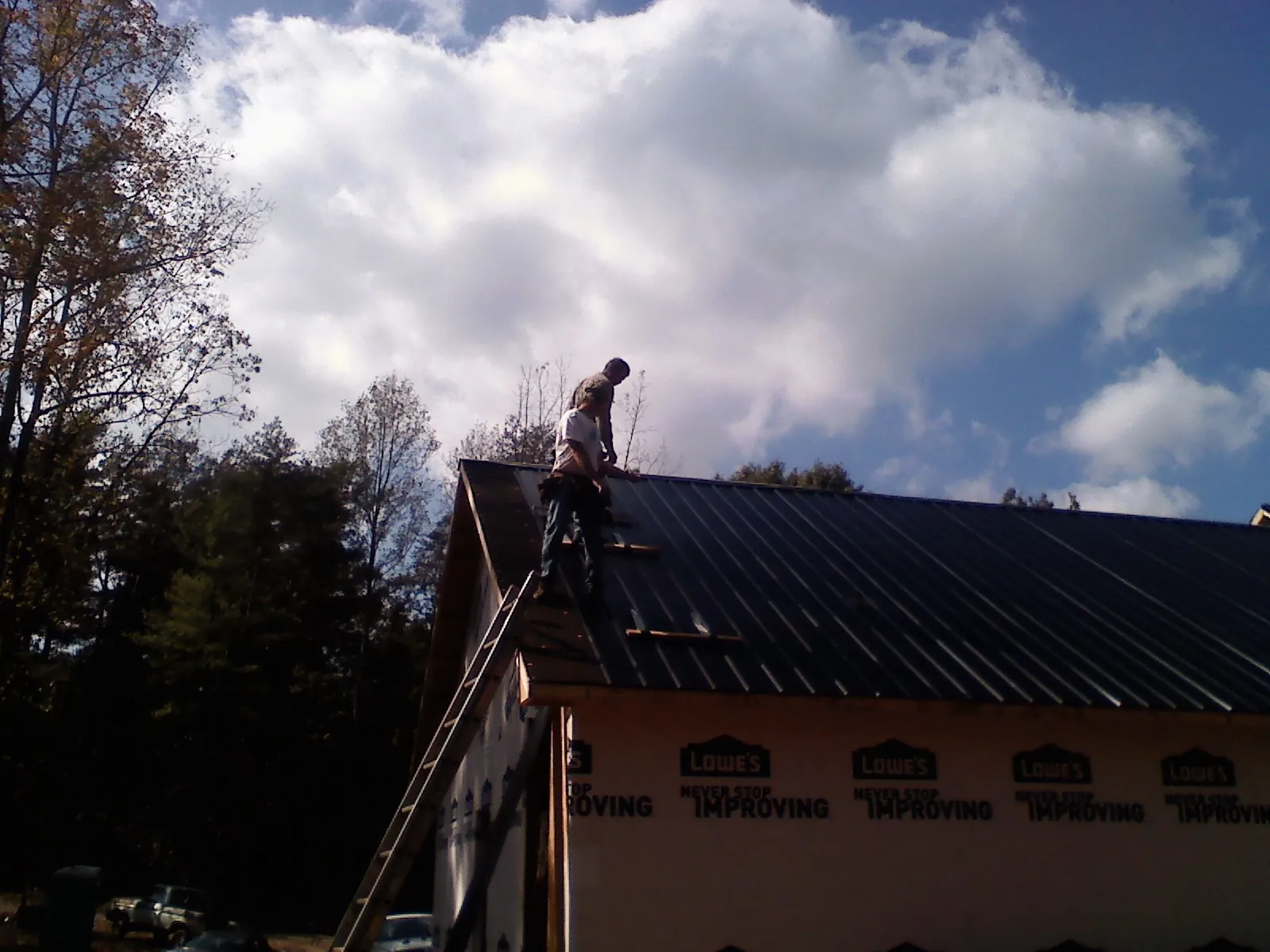 Roofer fastening dark metal panels high against a cloudy sky, from a Roof Inspection job in Dowagiac