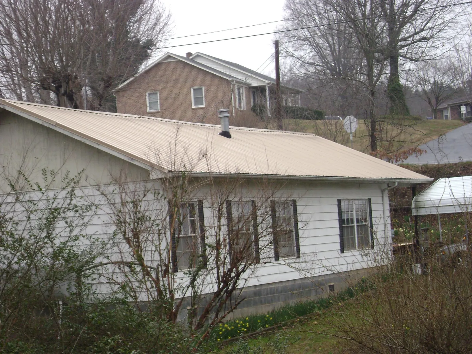Tan metal roof on a white sided house set into a hillside — Commercial Roofing by Roofing Brothers in Dowagiac